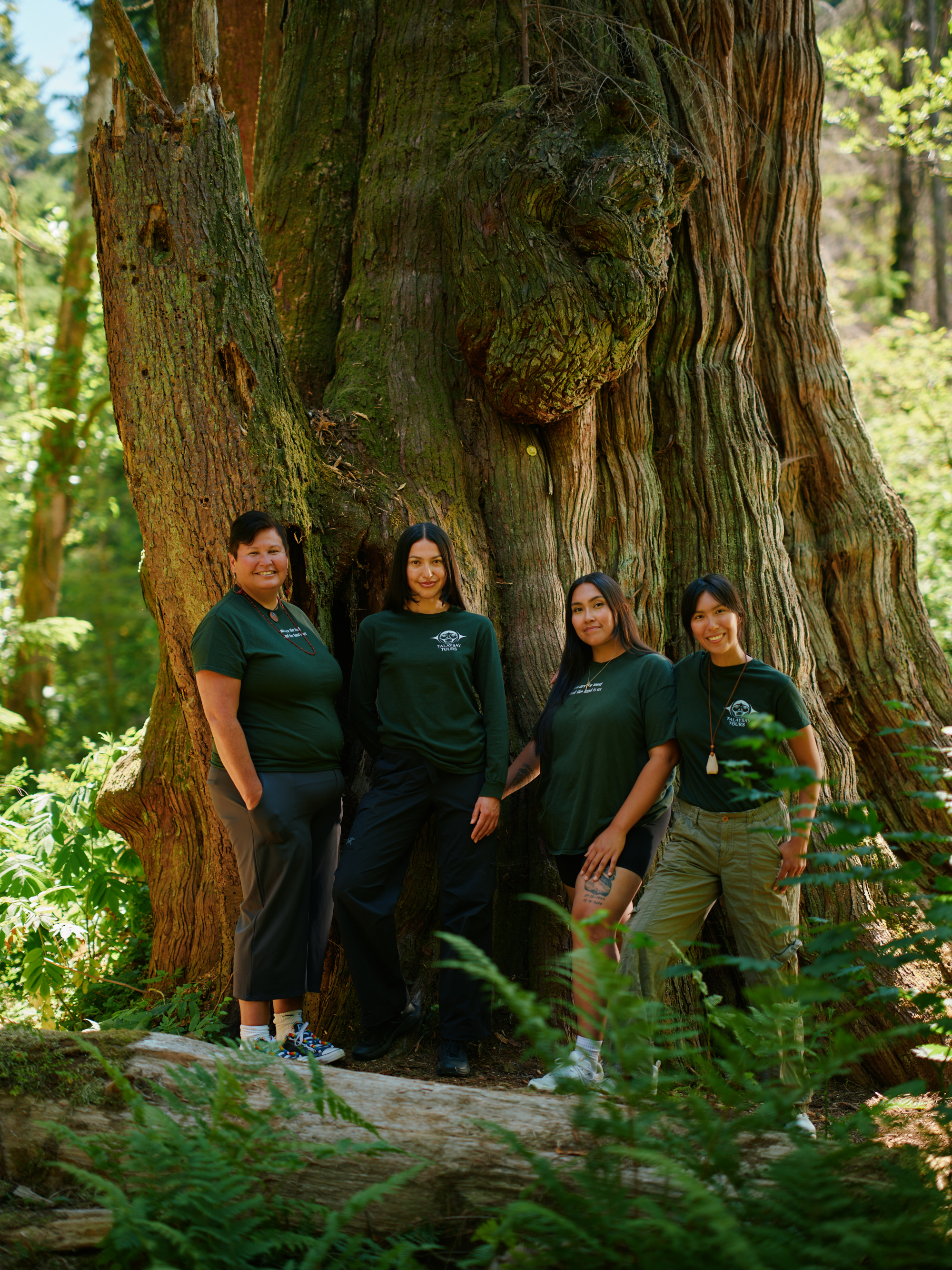 Four members of the Talaysay Tours team standing together beside a large tree in the forest.